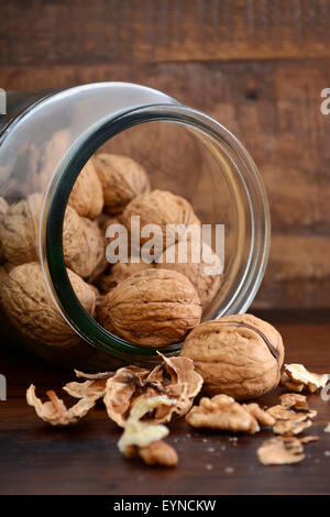 Le noci fresche in gusci di cadere fuori il vasetto di vetro su rustiche in legno scuro dello sfondo della tabella. Foto Stock