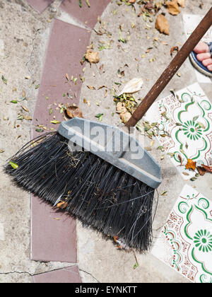 Scopa spazza figliata di foglia dal calcestruzzo marciapiede Foto Stock