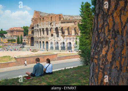 Colosseo Roma, vista in estate di una giovane coppia turistica seduto nel Parco del Celio di fronte al Colosseo nel centro di Roma, Italia. Foto Stock