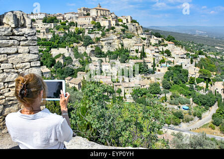 Donna che mantiene un ipad per comporre e scattare una foto della Scenic francese borgo collinare di Gordes Provenza nel sud della Francia Foto Stock