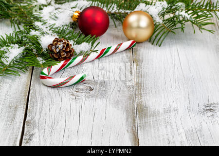 Candy Cane con coperta di neve vera Abete rami, ornamenti, il cono e la neve sul bianco rustico di tavole di legno. Stagione di Natale co Foto Stock