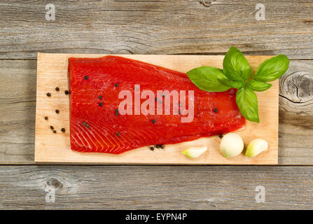 Vista superiore colpo di rosso fresco filetto di salmone sul cedro di cottura con scheda di Peppe, aglio e basilico. Legno invecchiato sotto. Foto Stock