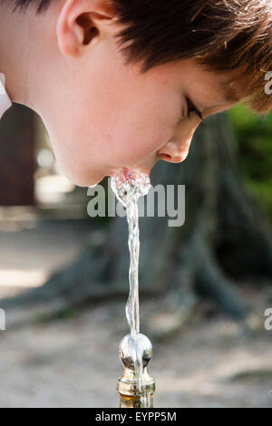 Bambino, ragazzo caucasico, 7-8 anni, chiudere fino al viso. La faccia rivolta verso il basso come sete ragazzo prende una bevanda di acqua da una pubblica fontana nel parco. Foto Stock