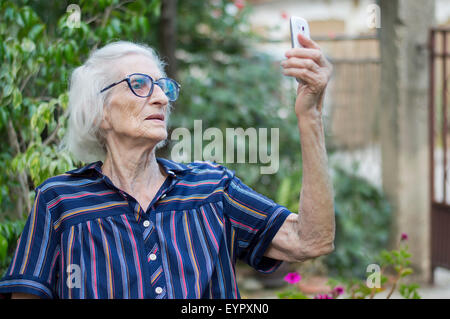 Novanta anni nonna prendendo un selfie con uno smartphone nel cortile. Abstract di comunicazioni Foto Stock