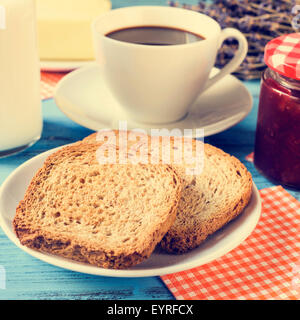 Primo piano di alcuni toast in una piastra, una tazza di caffè e una bottiglia di latte ed un vasetto di marmellata su un rustico in legno di colore blu, tavolo con un cr Foto Stock