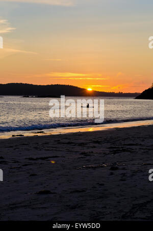 Bel tramonto in spiaggia di Mackenzie in Tofino. Persona seduta sulla scheda di racchetta e guardare il tramonto. Foto Stock