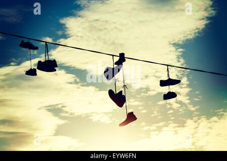 Vintage tonica sagome di scarpe appeso sul cavo al tramonto. Foto Stock