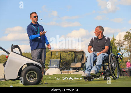 Uomo con una lesione del midollo spinale in un carrello adattativo circa a giocare a golf insieme con il suo assistente Foto Stock