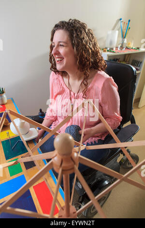 Donna con la distrofia muscolare a lavorare con il suo ombrello alzavetro del filato mentre nella sua sedia di potenza Foto Stock