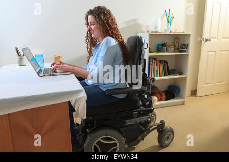 Donna con la distrofia muscolare in suo potere sedia usando il suo computer portatile nel suo ufficio Foto Stock