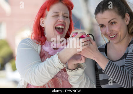 Non vedenti giovani donne utilizzando la tecnologia assistiva sui loro telefoni cellulari e ridere Foto Stock