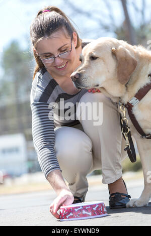 Giovane donna con una minorazione visiva alimentando il suo cane di servizio Foto Stock