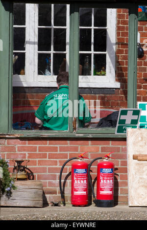 St John Ambulance persona siede con la schiena per la fotocamera in una piccola veranda Foto Stock