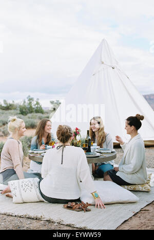 Il gruppo di donne gustando un pasto all'aperto da un teepee nel deserto. Foto Stock