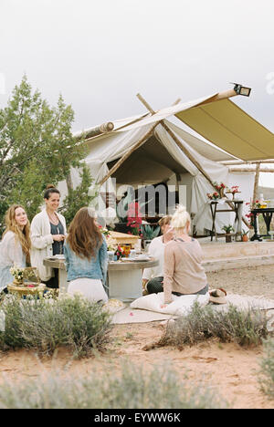 Il gruppo di donne amici seduti per terra intorno a un tavolo in un deserto, una tenda in background. Foto Stock