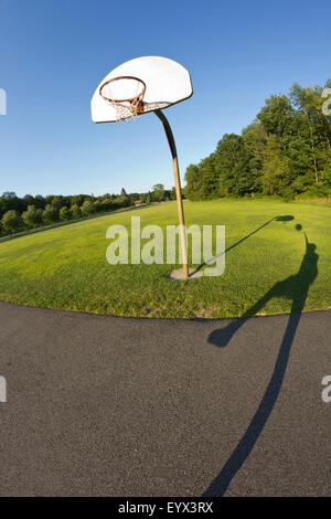 Silhouette di un giocatore di basket a sparare per il cerchio sulla corte esterna Foto Stock