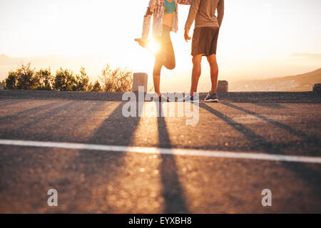 Ritagliato colpo di montare la coppia giovane in fase di riscaldamento prima di correre insieme a sunrise. Giovane uomo e donna di esercitare nella mattina. Foto Stock