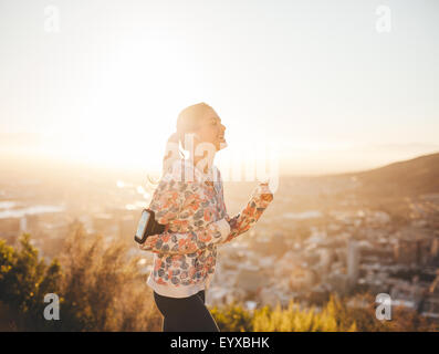 Colpo di montare femminile nella mattinata con la luce diretta del sole. Giovane donna all'aperto su una corsa sorridente. Foto Stock