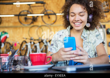 Donna sorridente con cuffie sms sul cellulare in bike shop Foto Stock