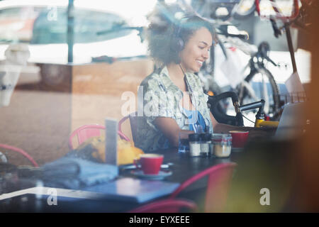Donna sorridente con le cuffie collegate al computer portatile in cafe Foto Stock