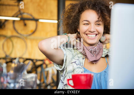 Donna sorridente al computer portatile in bike shop regolazione collo sciarpa Foto Stock