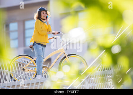 Donna sorridente parlando al cellulare in bicicletta in città Foto Stock