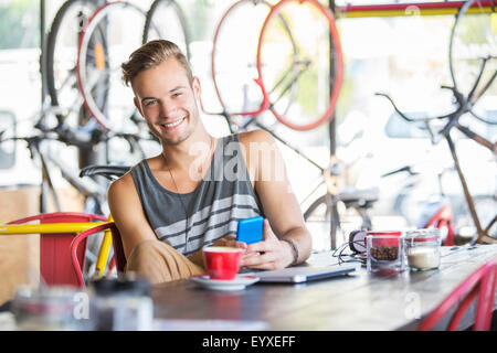 Ritratto uomo sorridente con caffè e telefono cellulare in negozio di biciclette Foto Stock