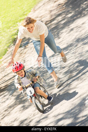 Madre figlio di spinta con il casco in bicicletta nel parco di sole Foto Stock