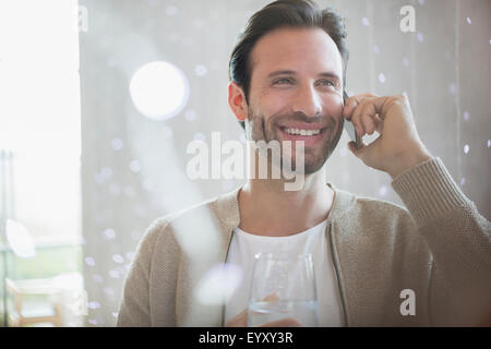 Uomo sorridente acqua potabile e parlando al cellulare Foto Stock