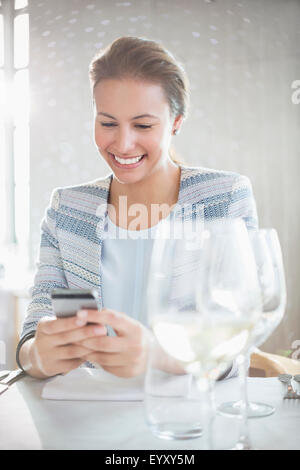 Donna sorridente texting con un telefono cellulare al ristorante tabella Foto Stock