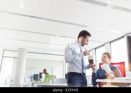 Imprenditore e imprenditrice mangiare asporto cinese con bacchette in office Foto Stock