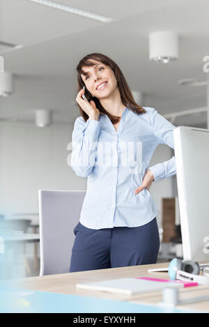 Brunette imprenditrice parlando al cellulare alla scrivania in ufficio Foto Stock