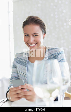 Ritratto fiducioso imprenditrice texting con un telefono cellulare al ristorante tabella Foto Stock