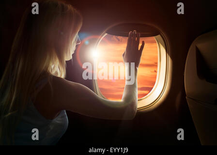 La donna caucasica ammirando il tramonto dalla finestra di aeroplano Foto Stock