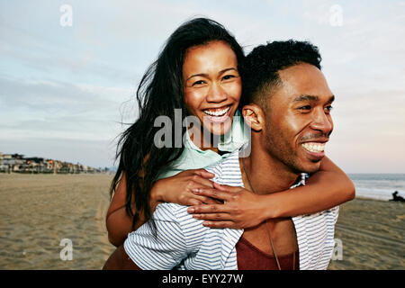 Uomo che porta la fidanzata piggyback sulla spiaggia Foto Stock