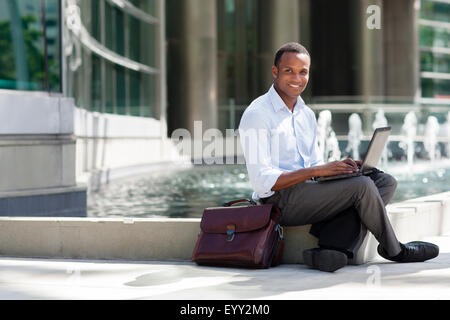 Imprenditore nero utilizzando laptop vicino Fontana urbano Foto Stock