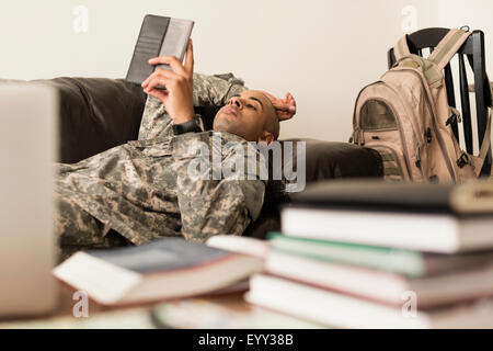 Razza mista soldato utilizzando digitale compressa sul divano vicino a libri Foto Stock