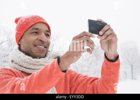 Uomo nero utilizzando il cellulare in neve Foto Stock