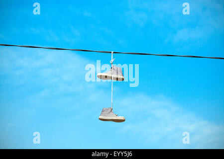 Vecchie scarpe appeso a un cavo elettrico contro il cielo blu. Foto Stock