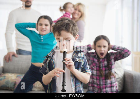 Famiglia caucasica che copre le orecchie con ragazzo giocando recorder Foto Stock
