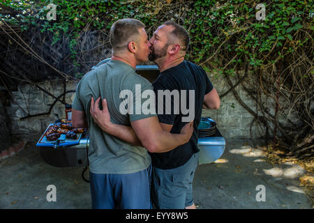 Coppia gay baciare e grigliare cibo nel cortile posteriore Foto Stock