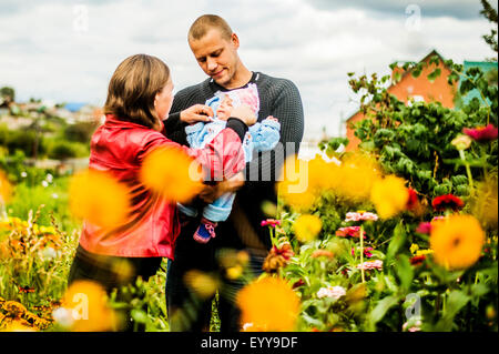 I genitori caucasici holding baby vicino a fiori Foto Stock