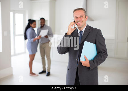 Agente immobiliare parlando al cellulare con il giovane nella nuova casa Foto Stock