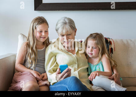 Nonna caucasica e nipoti tramite telefono cellulare sul divano Foto Stock