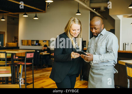 Cameriere e imprenditrice utilizzando i telefoni cellulari in cafe Foto Stock