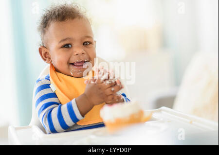 Razza mista baby boy eating in sedia alta Foto Stock