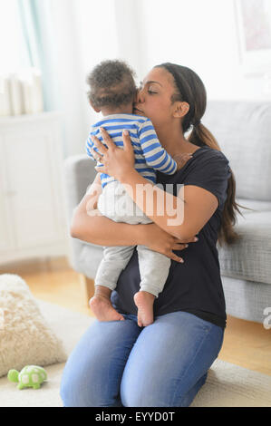 Razza mista madre kissing baby figlio nel soggiorno Foto Stock