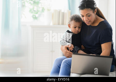 Razza mista madre utilizzando laptop con baby figlio nel soggiorno Foto Stock