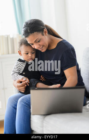 Razza mista madre utilizzando laptop con baby figlio nel soggiorno Foto Stock