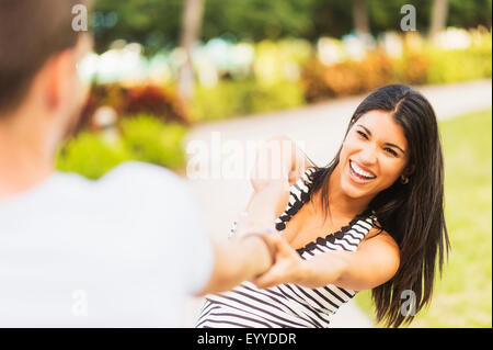 Sorridente ragazza ispanica tirando il fidanzato in posizione di parcheggio Foto Stock